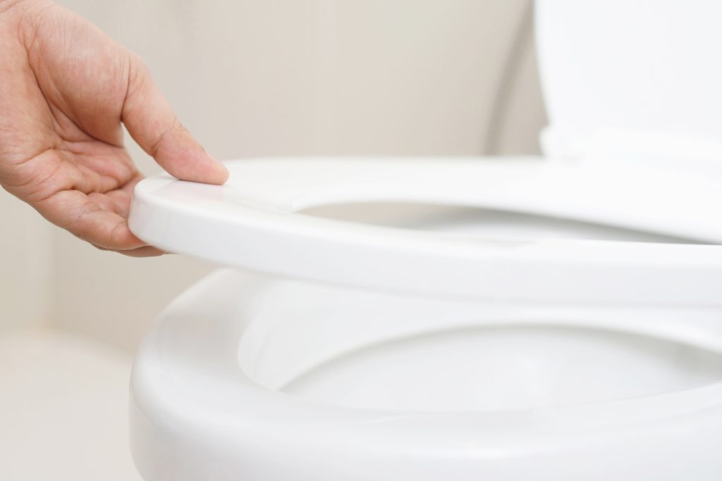 Closeup of a hand lifting a toilet seat