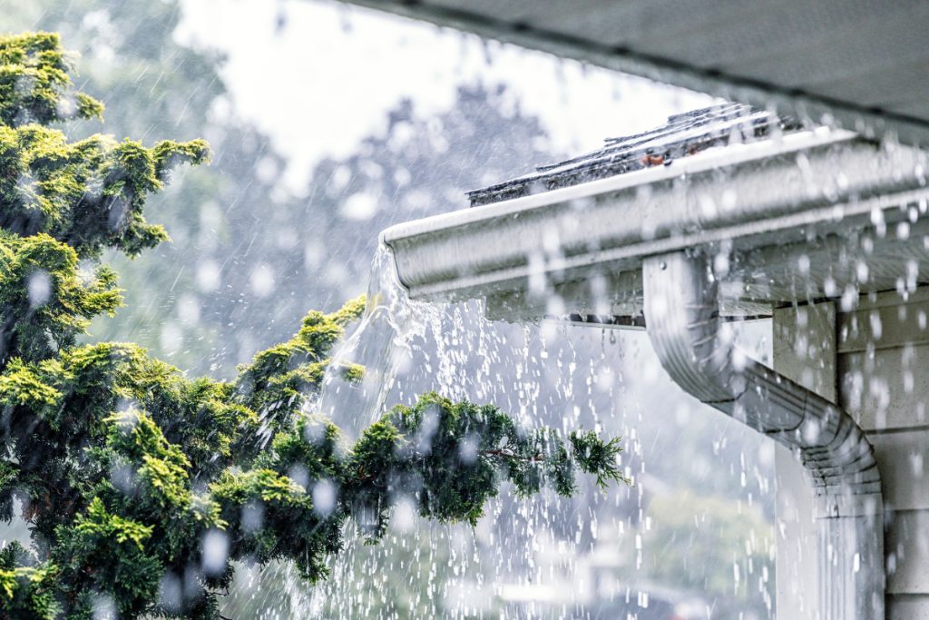 Close-up of rain falling on the corner of a roof and gutters.